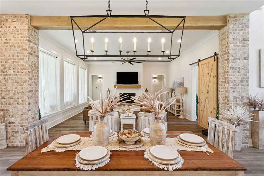Beyond the dining space, the seamless transition into the living room highlights the home’s thoughtful layout. A modern fireplace with a wooden mantle, statement ceiling fan, and sliding barn door tie together the farmhouse aesthetic with a contemporary twist. Wide-plank wood floors run throughout, enhancing the sense of warmth and continuity. Ideal for entertaining or family living, this open layout allows for effortless flow, making every moment—from quiet mornings to lively dinners—feel perfectly at home.