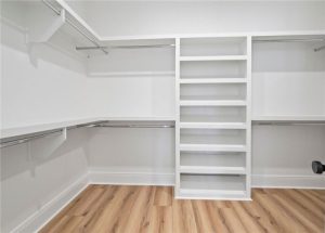 The image showcases a clean and organized walk-in closet with built-in white shelving and multiple hanging rods.