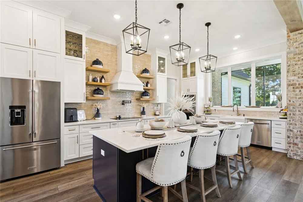 The oversized island, with contrasting dark cabinetry and designer pendant lighting, offers ample seating for casual meals or entertaining guests. Polished quartz countertops, a farmhouse sink overlooking large picture windows, and thoughtful touches like built-in storage and under-cabinet lighting complete the space. Every element—from the textures to the finishes—has been intentionally chosen to make this kitchen both inviting and inspiring, ideal for gathering, cooking, and creating memories.