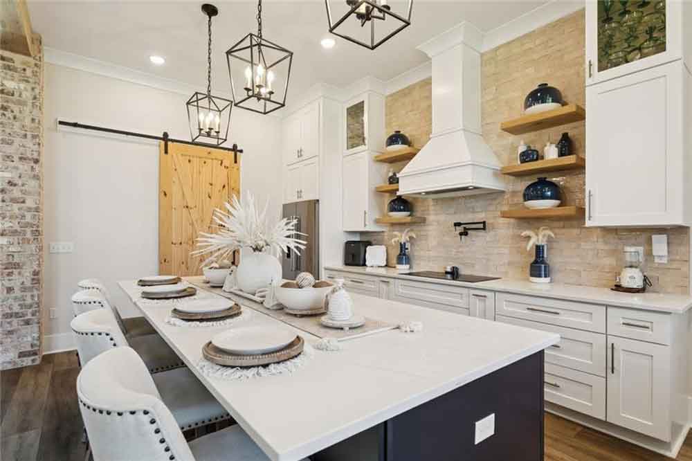 The oversized island, with contrasting dark cabinetry and designer pendant lighting, offers ample seating for casual meals or entertaining guests. Polished quartz countertops, a farmhouse sink overlooking large picture windows, and thoughtful touches like built-in storage and under-cabinet lighting complete the space. Every element—from the textures to the finishes—has been intentionally chosen to make this kitchen both inviting and inspiring, ideal for gathering, cooking, and creating memories.