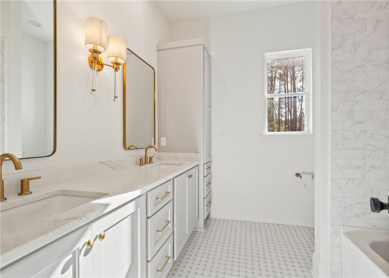 The image displays a refined bathroom featuring a double vanity with white cabinetry, marble countertops, and gold fixtures.
