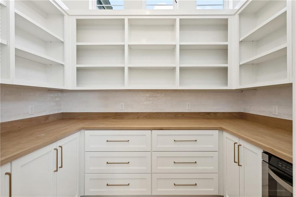 15-Shelving 1174 Audubon Pkwy This walk-in pantry features custom white cabinetry with sleek brass hardware and warm wood countertops, creating a clean yet inviting workspace.
