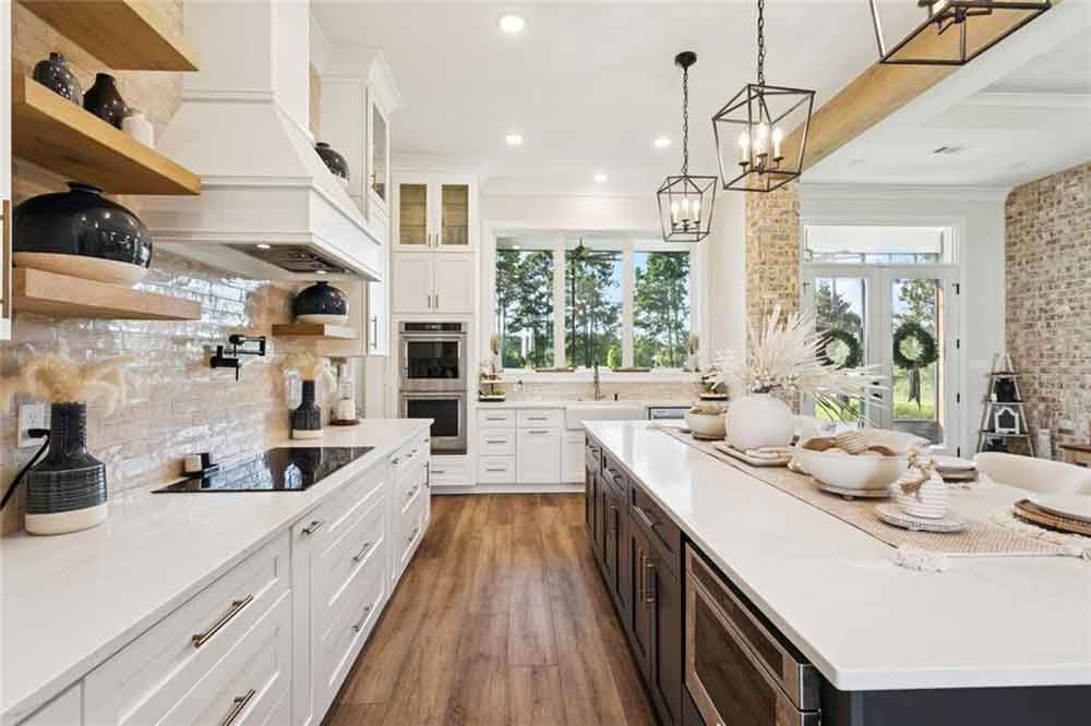 Every element is curated for both beauty and performance: from the custom vent hood and open wood shelving to the integrated double ovens and farmhouse sink. The clean lines of the cabinetry are elevated by elegant hardware and designer pendant lighting, while a pot filler and sleek cooktop make cooking effortless. With a clear view through to the dining and living areas—and easy access to the outdoors—this kitchen is the true heart of the home, perfectly designed for entertaining, gathering, and everyday luxury.