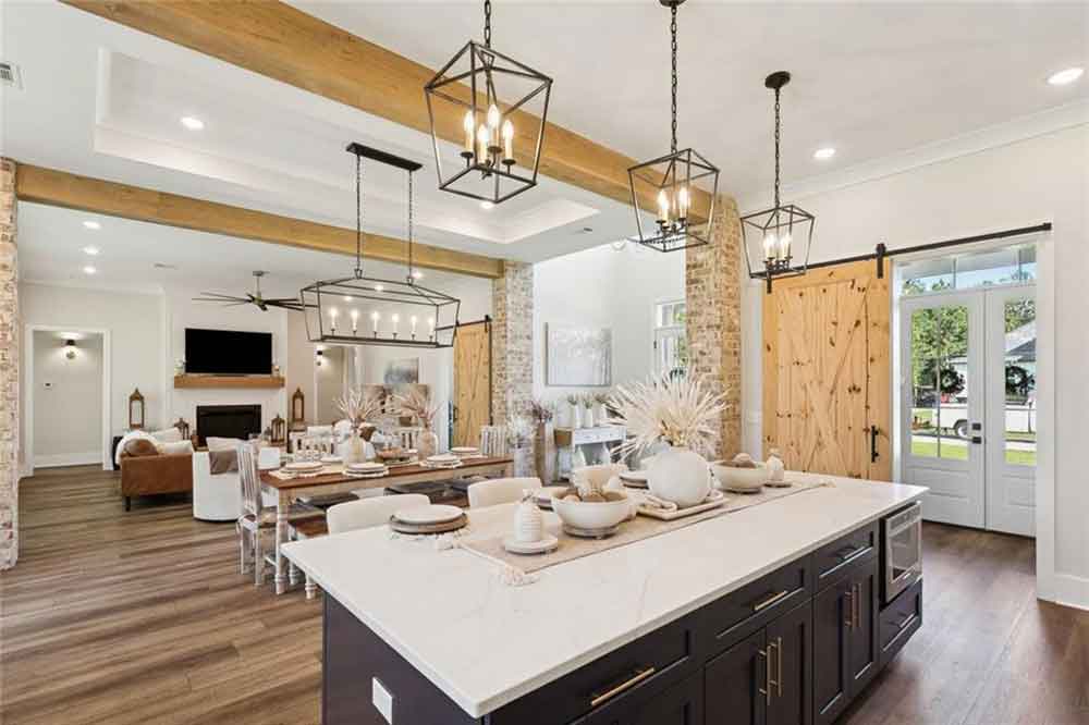 The living room completes this beautifully cohesive space, anchored by a sleek fireplace with a wooden mantle and surrounded by comfortable seating that encourages gathering. Wide-plank flooring, a sliding barn door, and abundant windows tie together the home’s sophisticated yet welcoming aesthetic. Every detail—from the lighting to the layout—has been thoughtfully curated to create a home that feels both elevated and deeply comfortable.