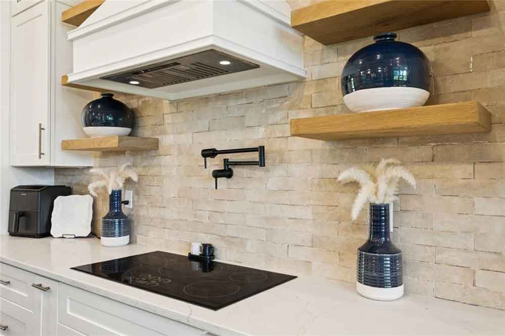 Decorative navy-and-white vases and subtle organic accents create a touch of artistry, balancing the modern elements with timeless charm. Under-cabinet lighting enhances both the texture of the backsplash and the elegance of the space, proving that every detail—from materials to lighting—was chosen with care to create a kitchen that’s both beautiful and highly functional.
