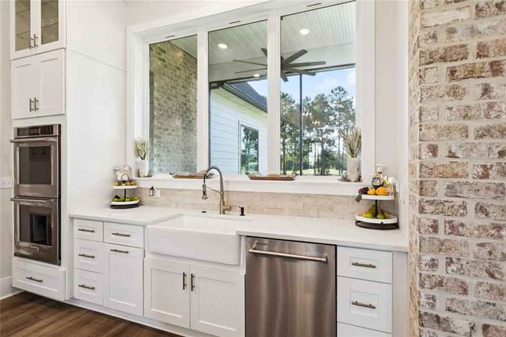 To the left, built-in double ovens and tall cabinetry provide both functionality and visual balance, while stainless steel finishes add a sleek modern touch. Thoughtful styling—like tiered trays, greenery, and soft neutral décor—adds personality without cluttering the space. This section of the kitchen perfectly complements the home’s open flow, blending modern convenience with timeless farmhouse character.