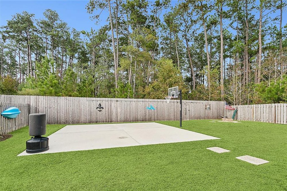 21 -3033 Lost Lake Basketball Court The fenced perimeter creates a secluded environment, while the lush green artificial grass contrasts with the natural tree line in the background.