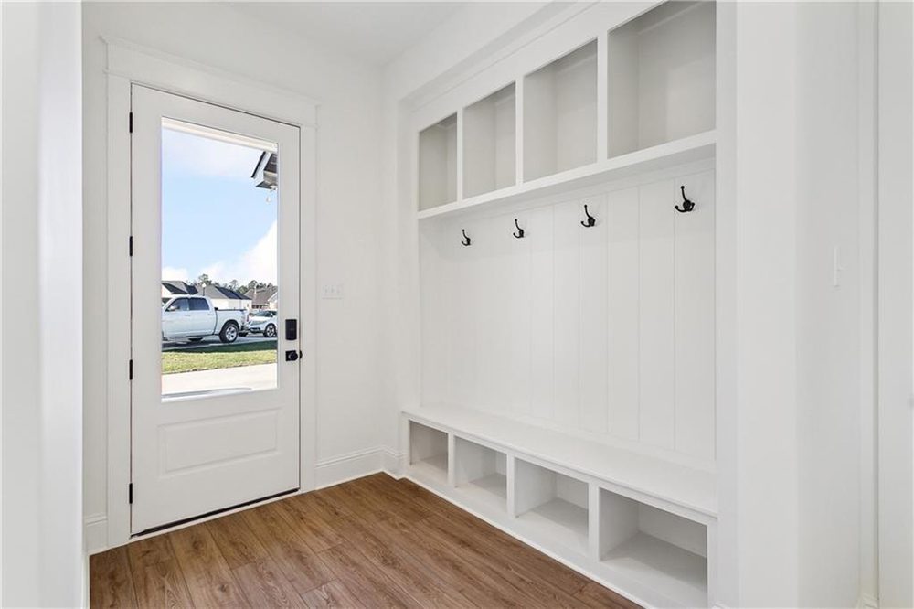 21-Mudroom 1174 Audubon Pkwy The natural wood-look flooring adds warmth and durability, complementing the room’s clean, white aesthetic. A full-light exterior door with matte black hardware lets in ample natural light and offers a welcoming view of the driveway and front yard.