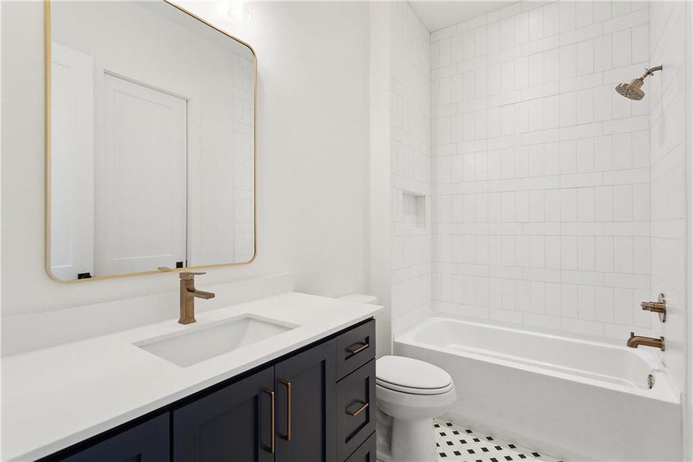 24-Custom Finishes 1174 Audubon Pkwy A bold black-and-white mosaic tile floor introduces subtle visual texture and ties together the high-contrast color palette. Gold fixtures in the shower add a cohesive, luxurious finish to this thoughtfully curated space that blends both form and function seamlessly.