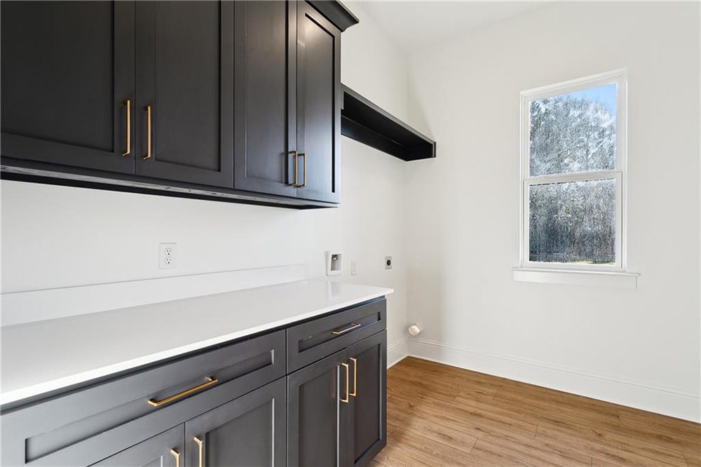 27-Laundry Room 1174 Audubon Pkwy This well-designed laundry room seamlessly combines utility and style. Featuring bold matte black cabinetry with sleek brass hardware, the space offers abundant storage both above and below a long stretch of gleaming white quartz countertop—perfect for folding laundry, storing supplies, or organizing household items.