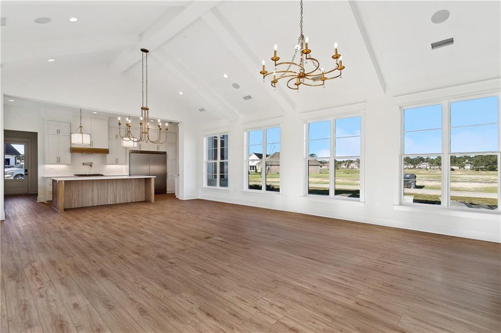 5- Hardwood Floor 1174 Audubon Pkwy This open-concept living area combines modern luxury with timeless elegance, featuring soaring vaulted ceilings adorned with twin gold chandeliers that add a touch of classic charm.