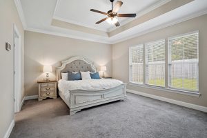 Master bedroom has trey ceilings and recessed lighting with plush carpeting.