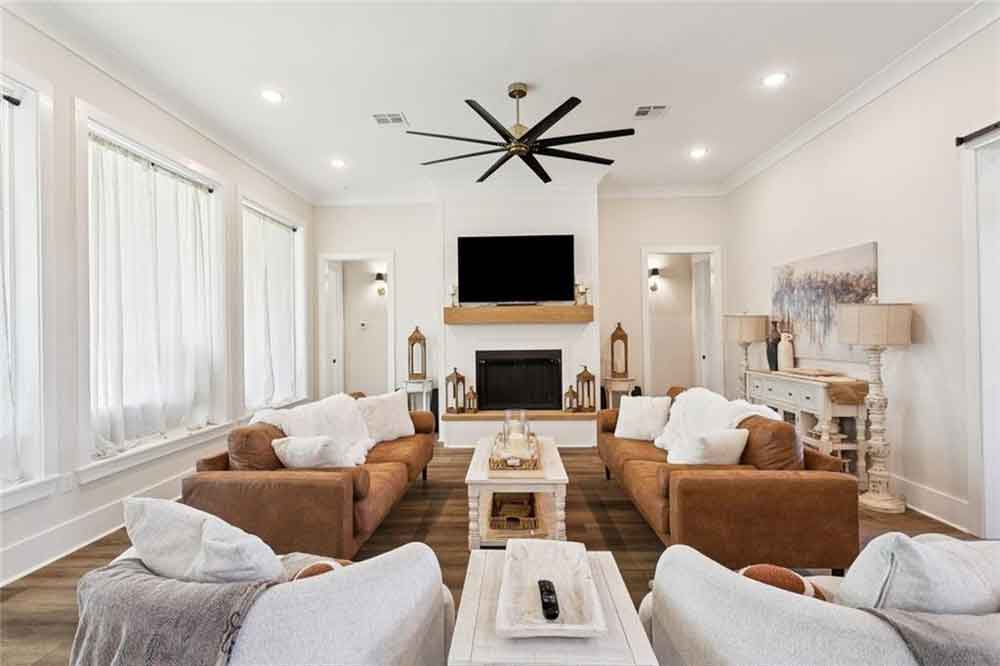 Bright and inviting living room featuring a cozy fireplace with a wood mantel, mounted TV, and abundant natural light streaming through multiple tall windows.