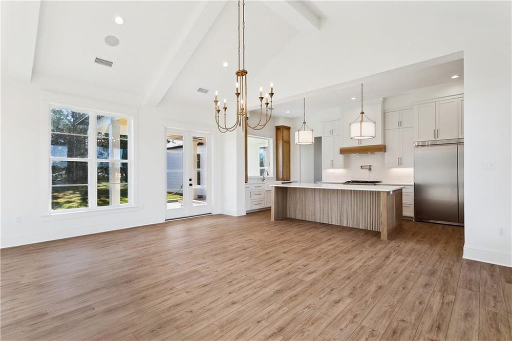 7-Custom Lighting 1174 Audubon Pkwy This bright and open-concept kitchen and dining area features vaulted ceilings, elegant chandeliers, and wide-plank wood flooring that adds warmth throughout the space.