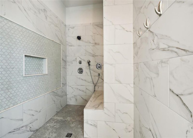 The use of different shapes and sizes of marble tiles adds texture and depth to the space, while built-in niches provide practical storage for toiletries.